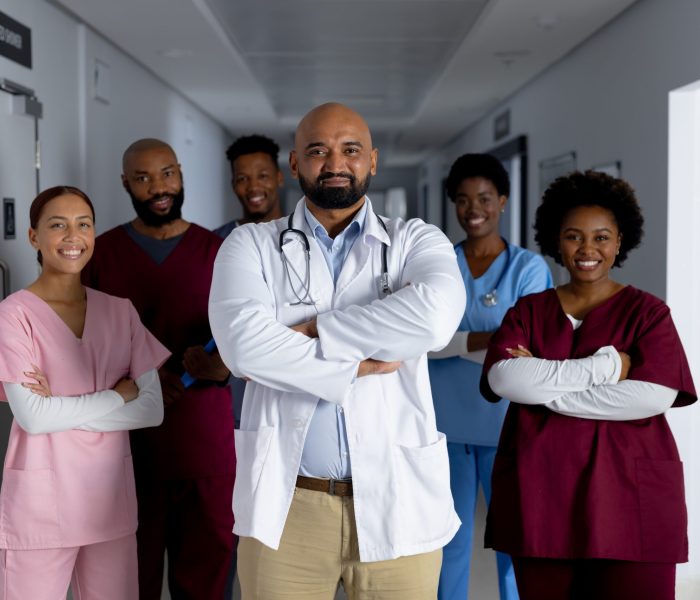 Portrait of happy diverse doctors standing in corridor at hospital. Hospital, medicine, teamwork, healthcare and work, unaltered.